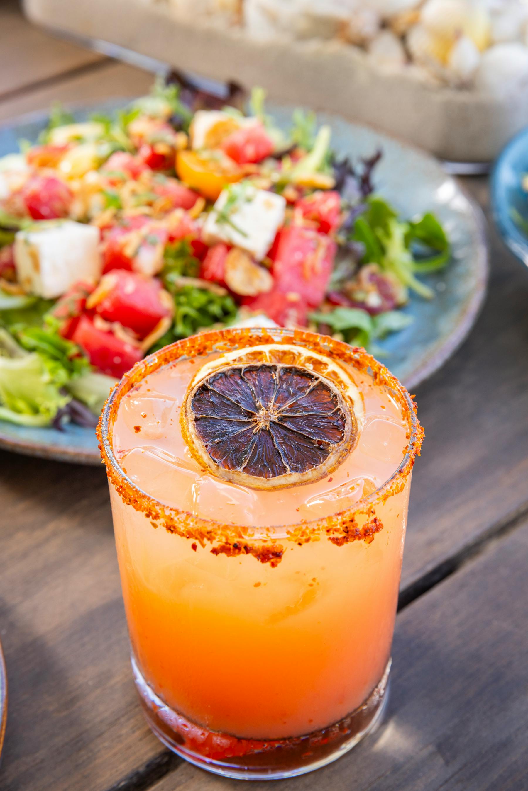 a glass of orange juice with a slice of lemon on top of a plate of salad