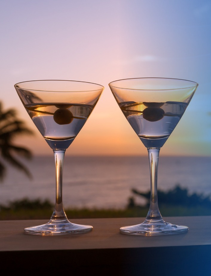 Two martinis with sunset, sea and palm tree views in the background