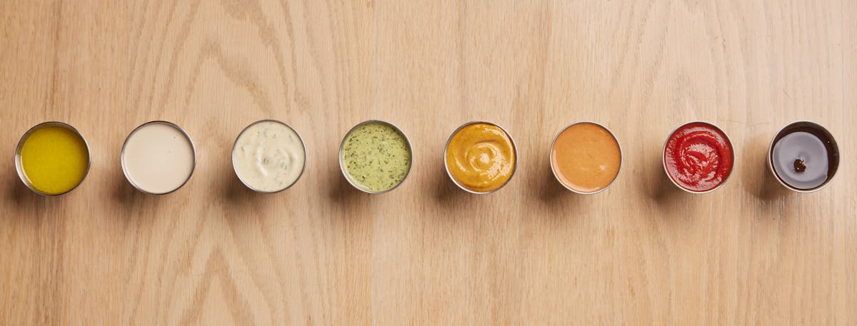 a collection of sauces in ramekins arranged in a row on a table
