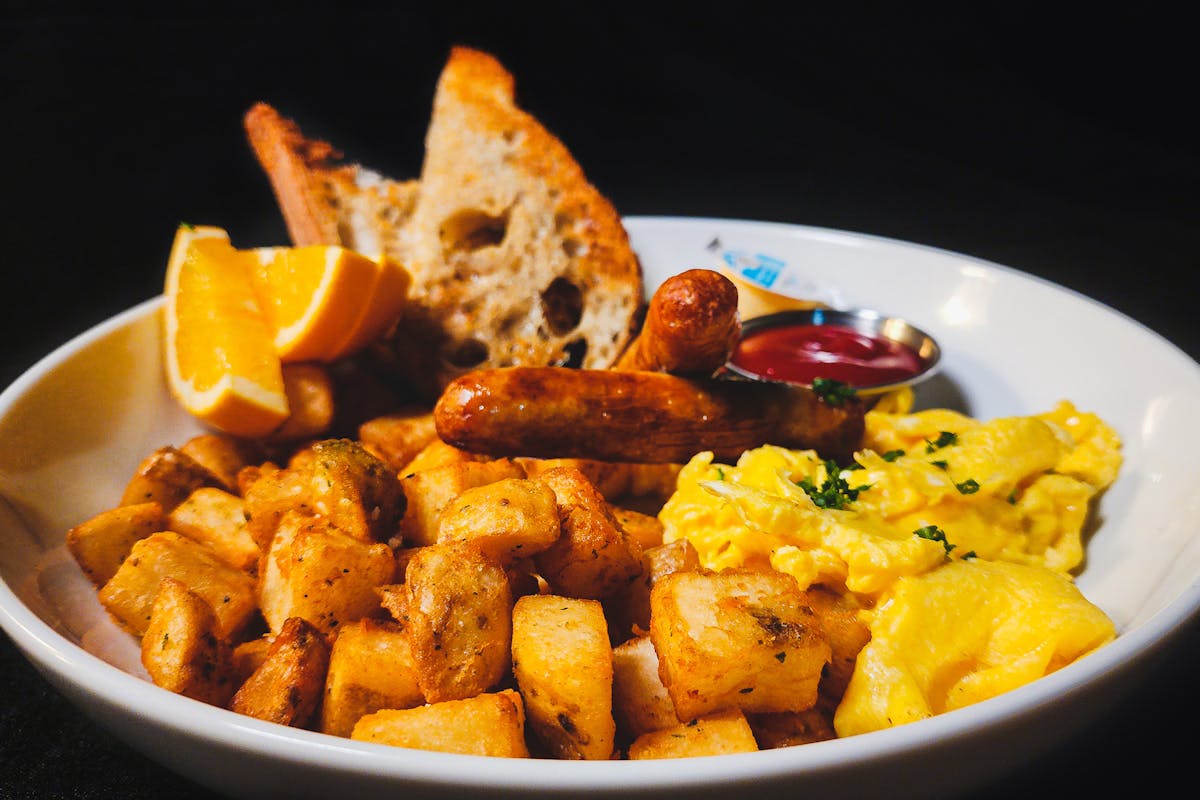 A hearty plate of hash browns, scrambled eggs, sausages, sourdough toast, and orange slices