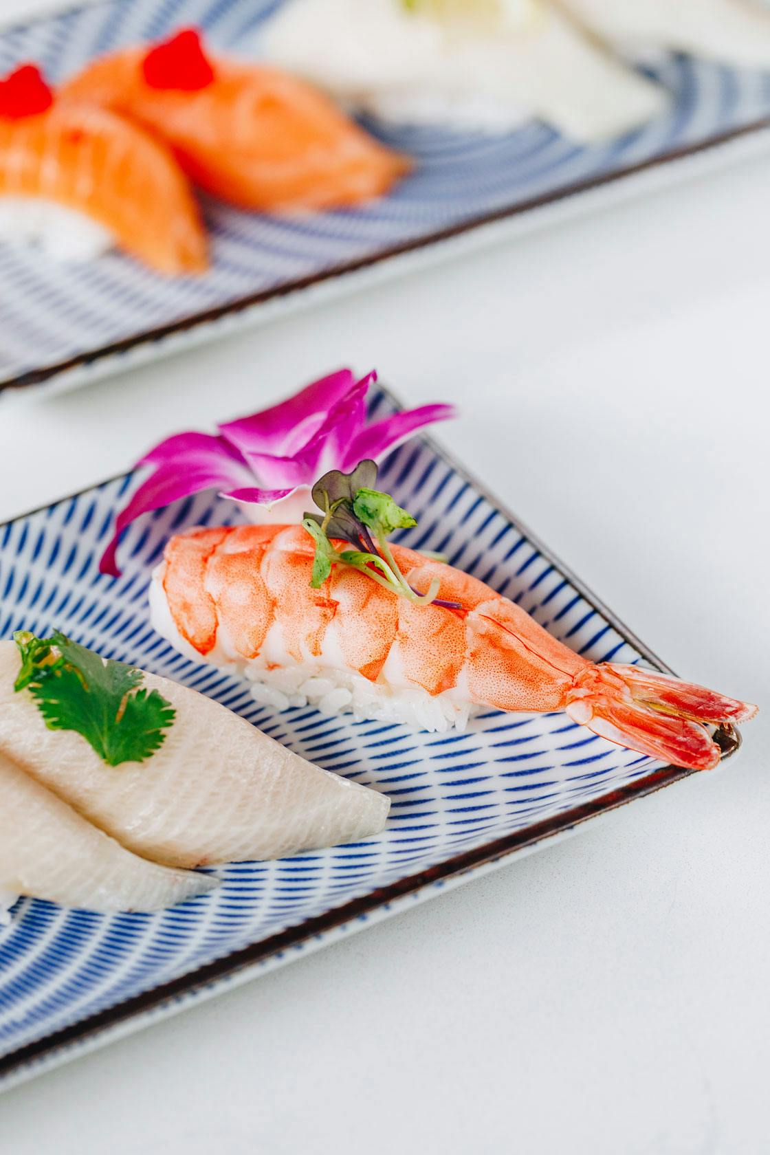 a big shrimp topped with cilantro sitting on a plate beside some fish