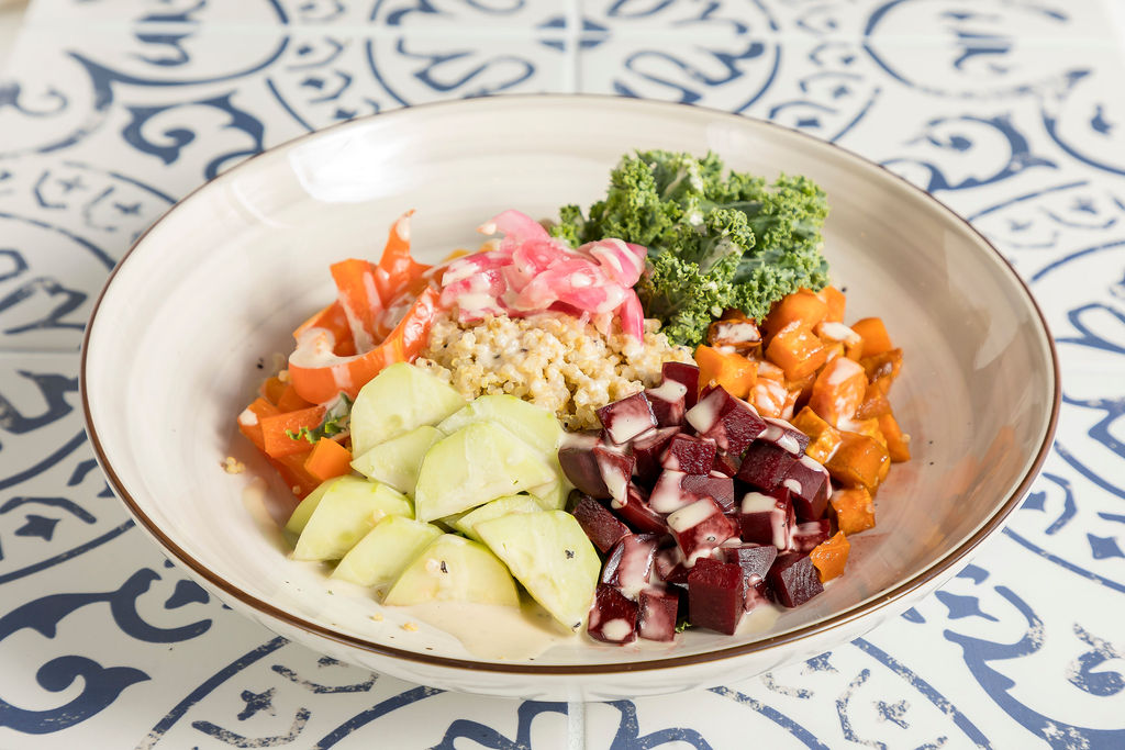 a bowl of Quinoa, avocado, chickpeas, kale, sweet potato, cucumber, red bell pepper, roasted beets, pickled onions, tahini drizzle, sunflower seeds