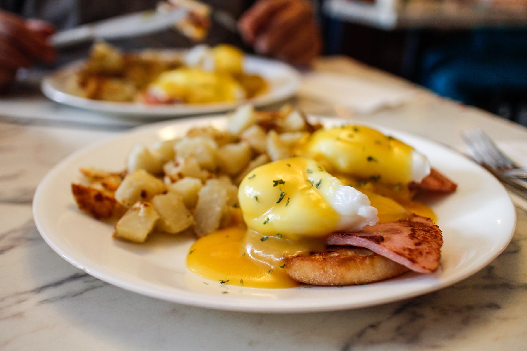a photo of two eggs benedicts with potatoes on the side
