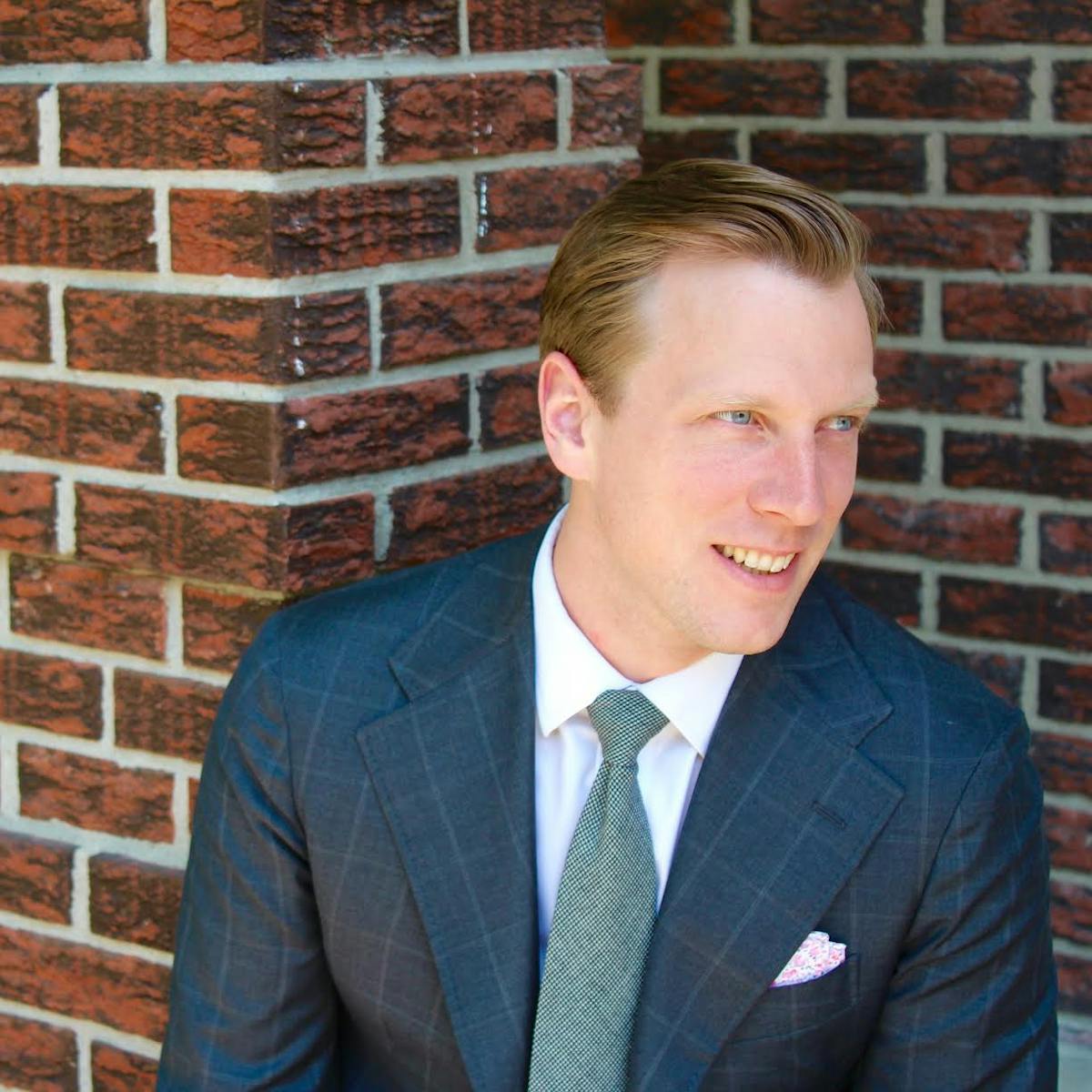 a man in a suit standing in front of a brick wall