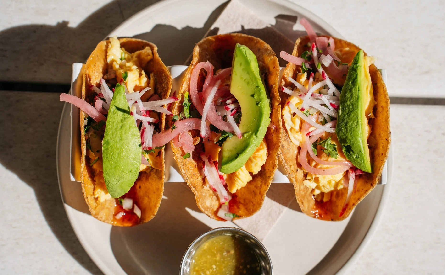 a plate of three tacos with a side of salsa