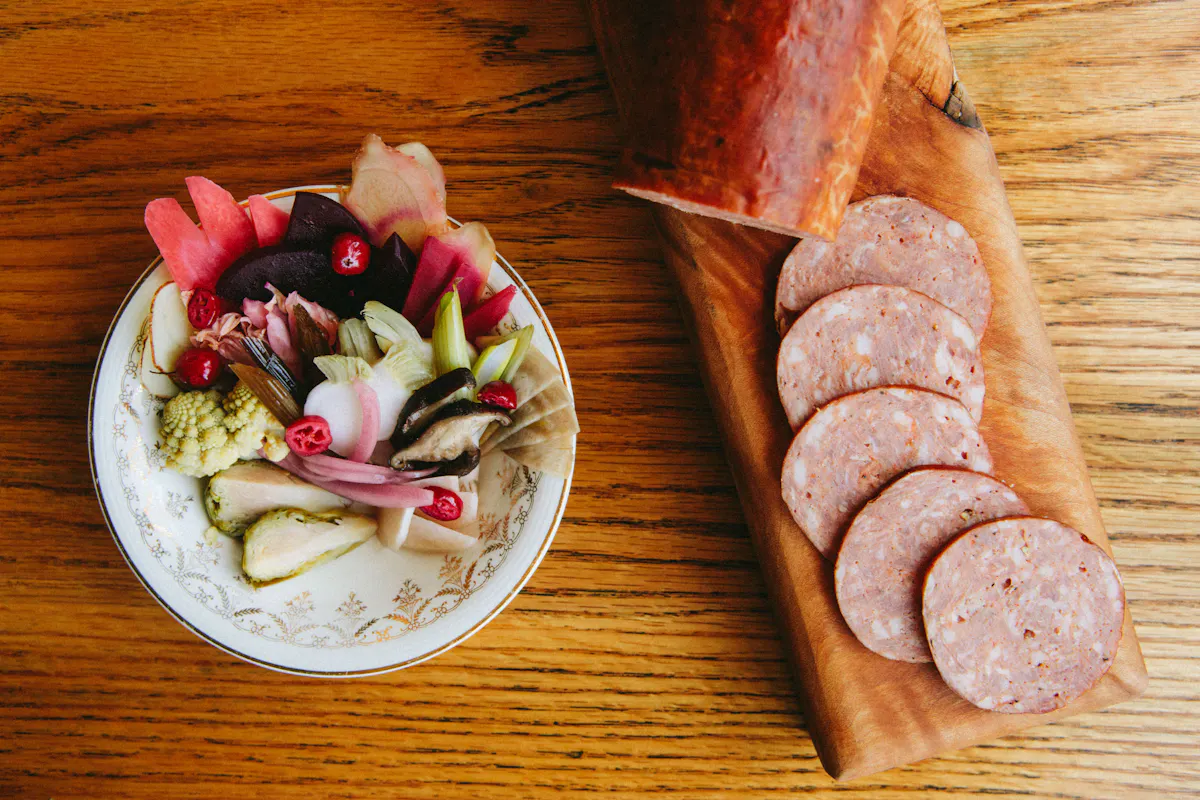 House made pickles and sliced sausage on a wooden table