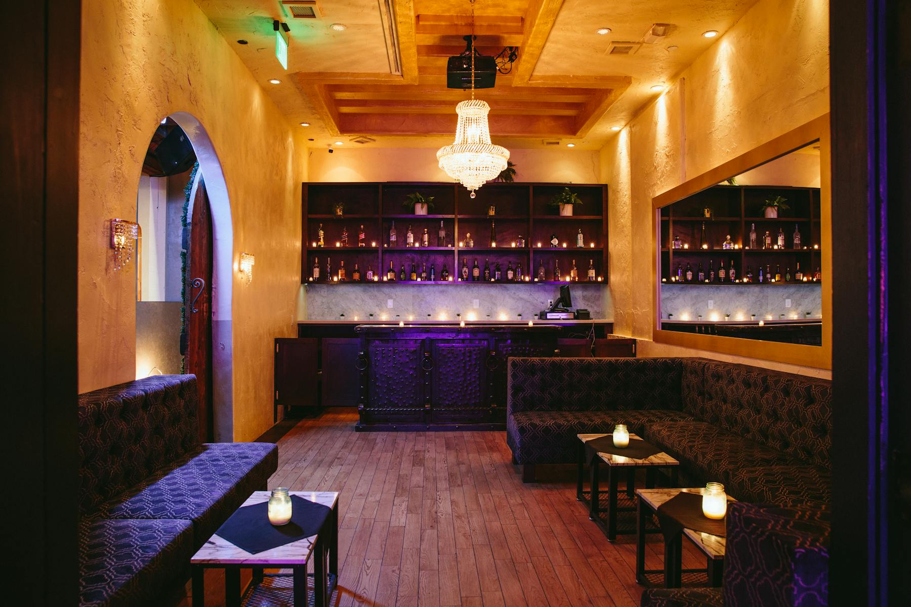 a big room with a bar, a shelf full of bottles, a table booth and a chandelier