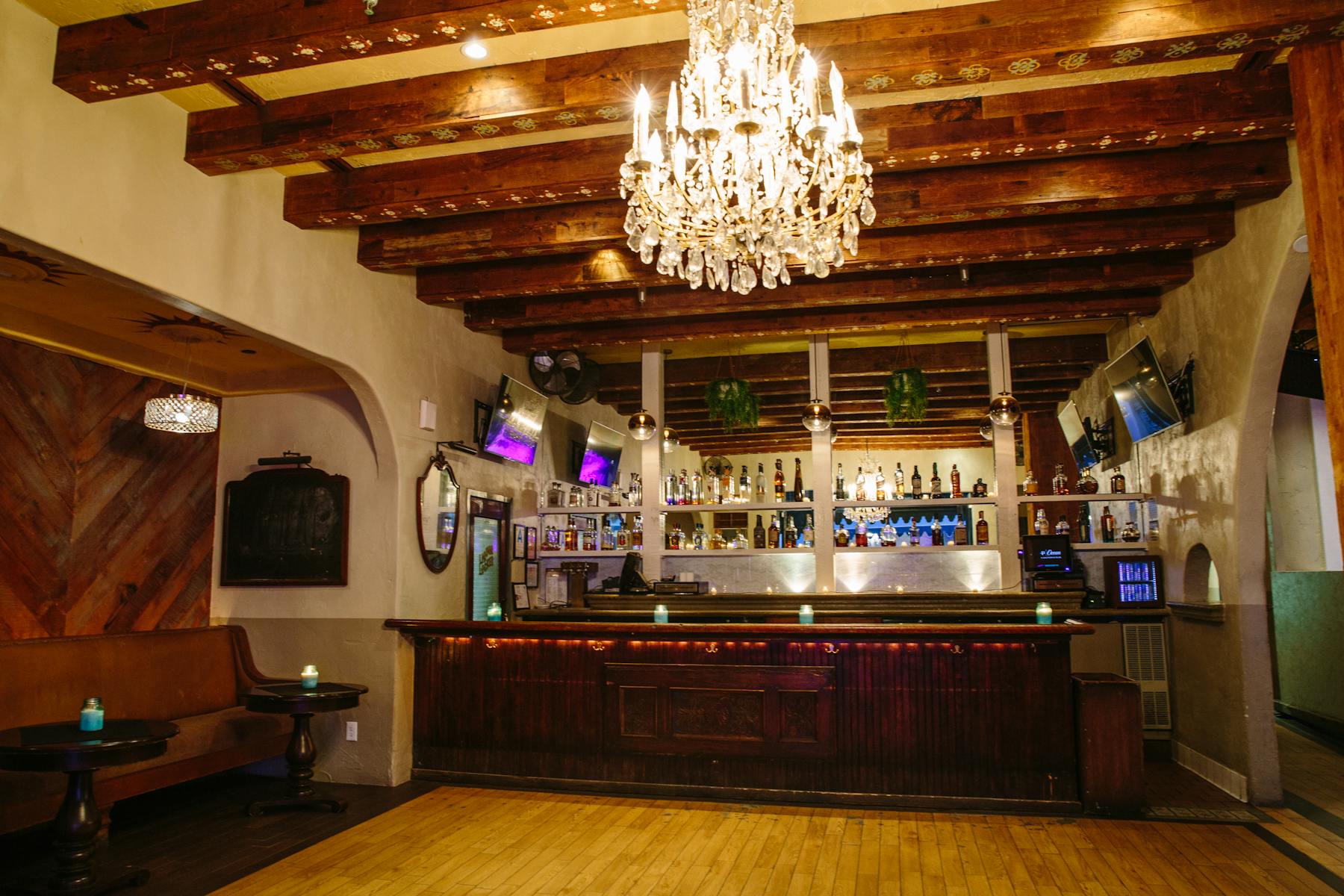 a large room with a yellow carpet filled with a bar, counter, a shelf topped with bottles and a chandelier