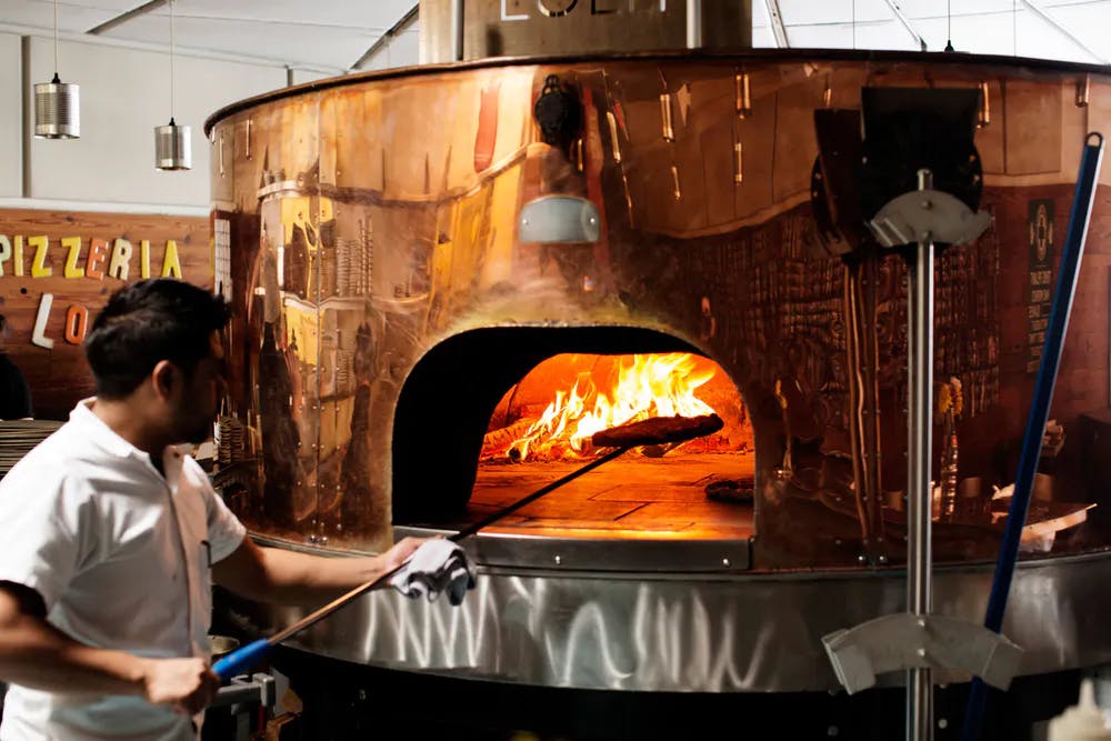 a man cooking pizza on a fire wood oven
