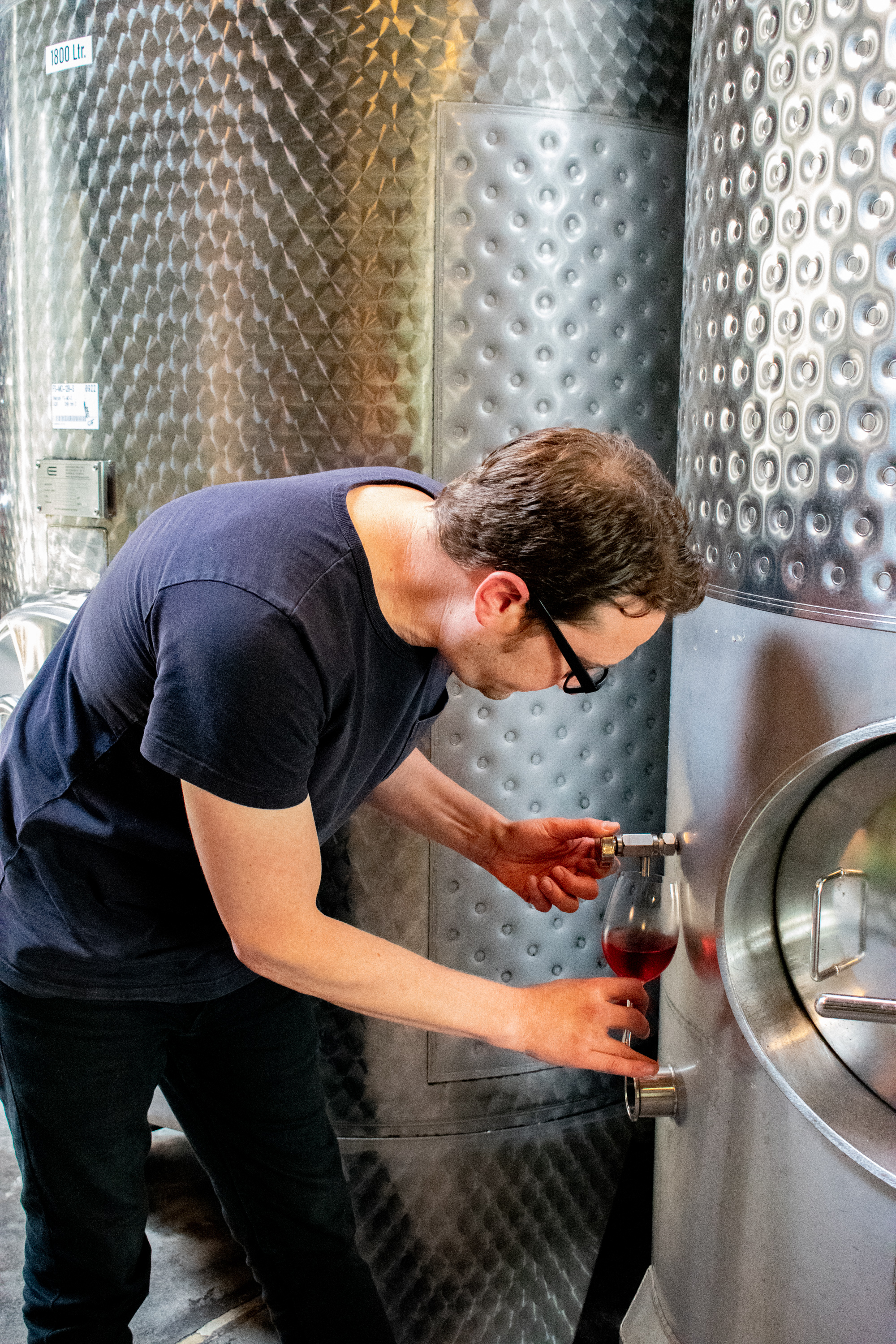 a winemaker pours a sample of wine from a steel tank