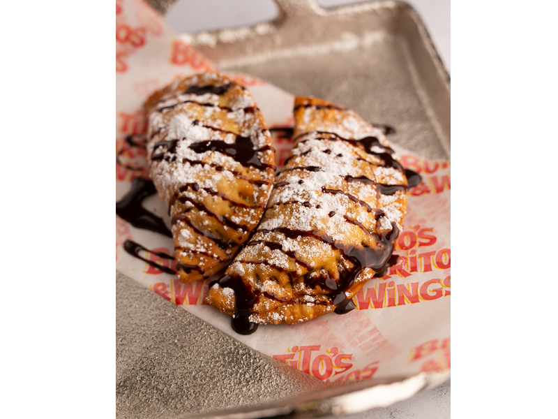 Cookie dough empanadas on a silver tray. The empanadas have been drizzled with chocolate sauce