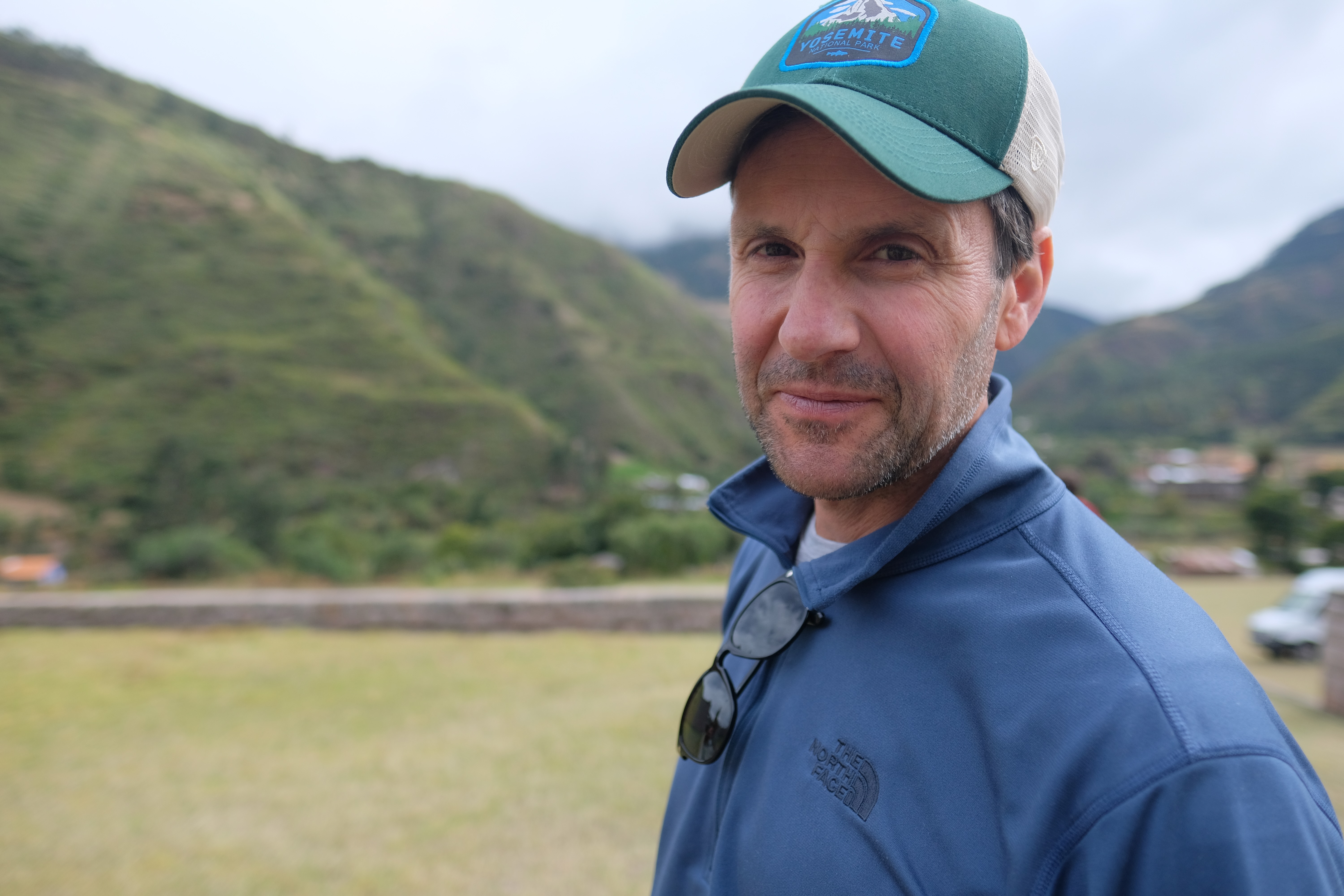 a man wearing a hat and sunglasses with a mountain in the background