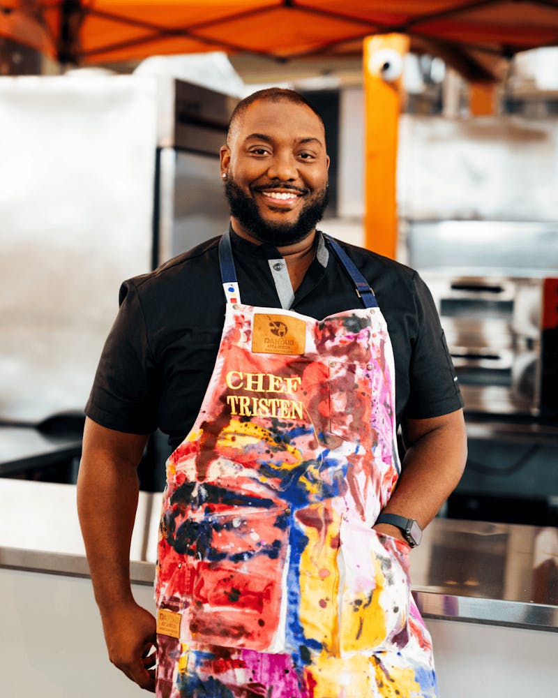 Chef Tristen Epps-Long standing in the kitchen wearing a chef apron labeled ‘Chef Tristen’.