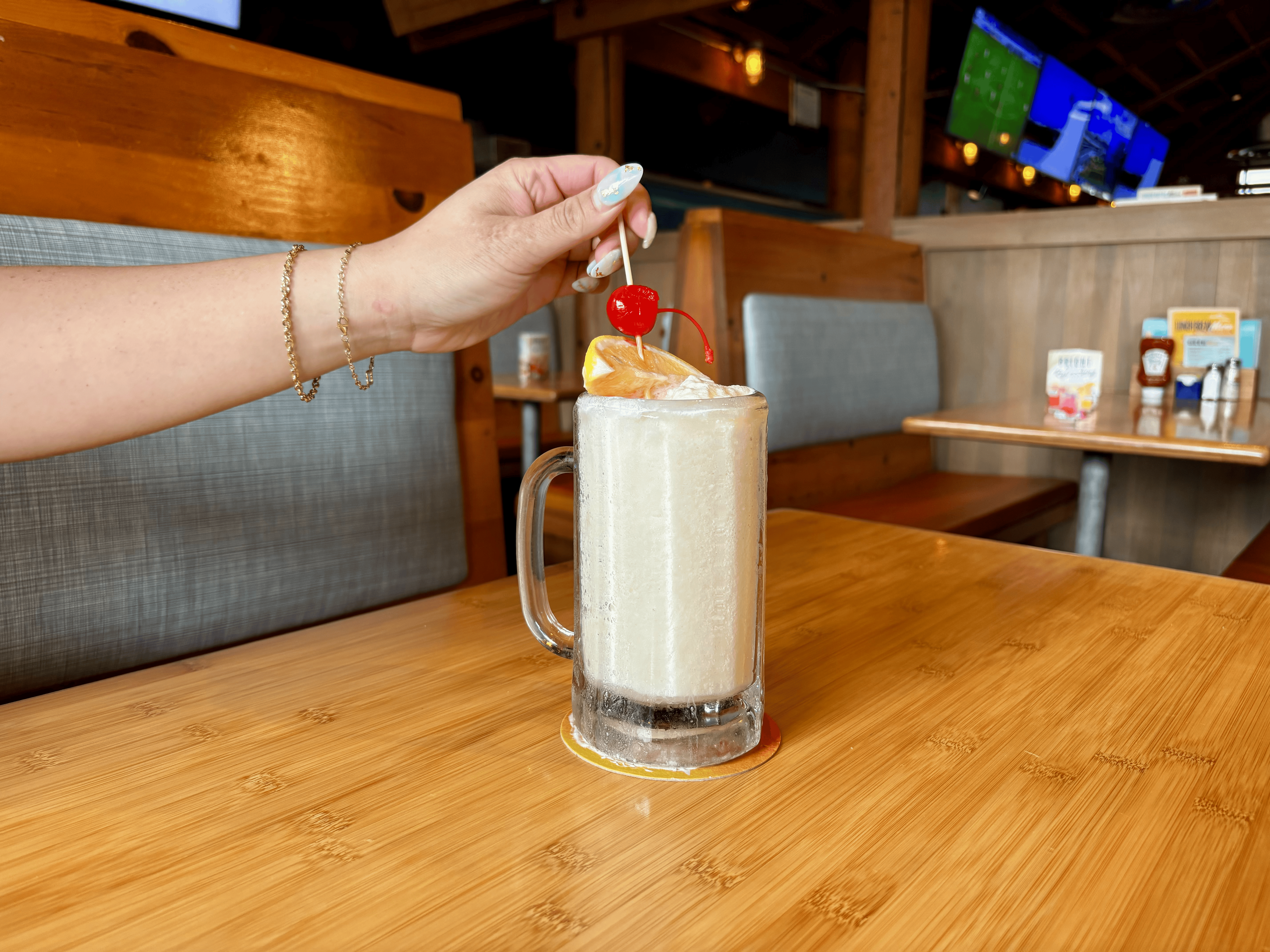 a person sitting at a wooden table drinking a Lemon Freeze with an orange and cherry in the drink