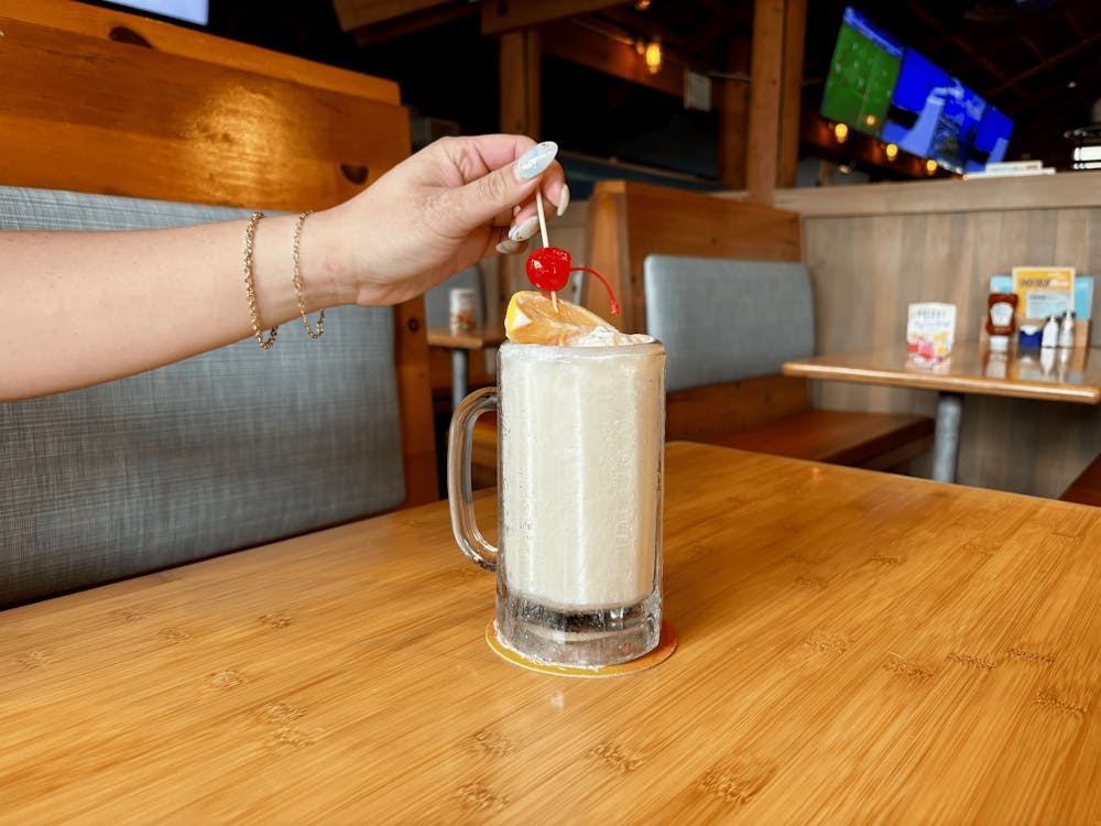 a person sitting at a wooden table drinking a Lemon Freeze with an orange and cherry in the drink