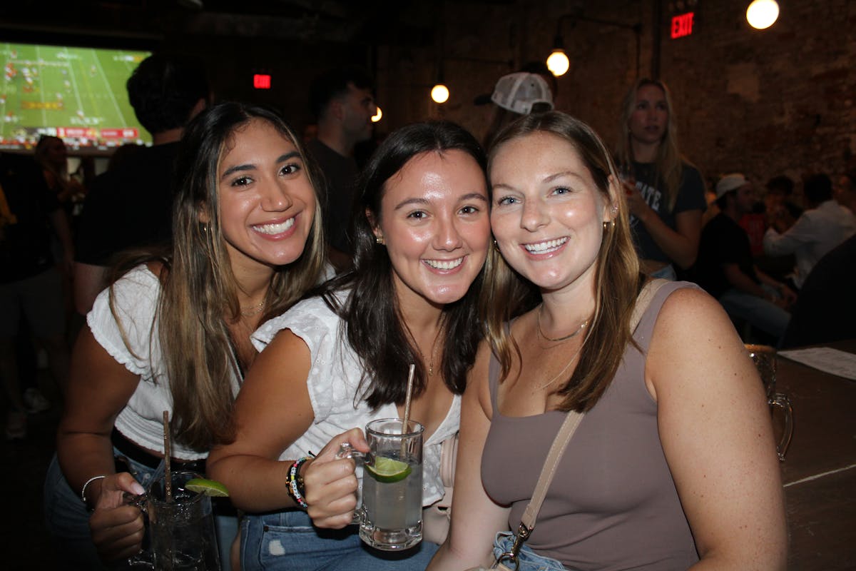 a group of girls holding drinks at a bar