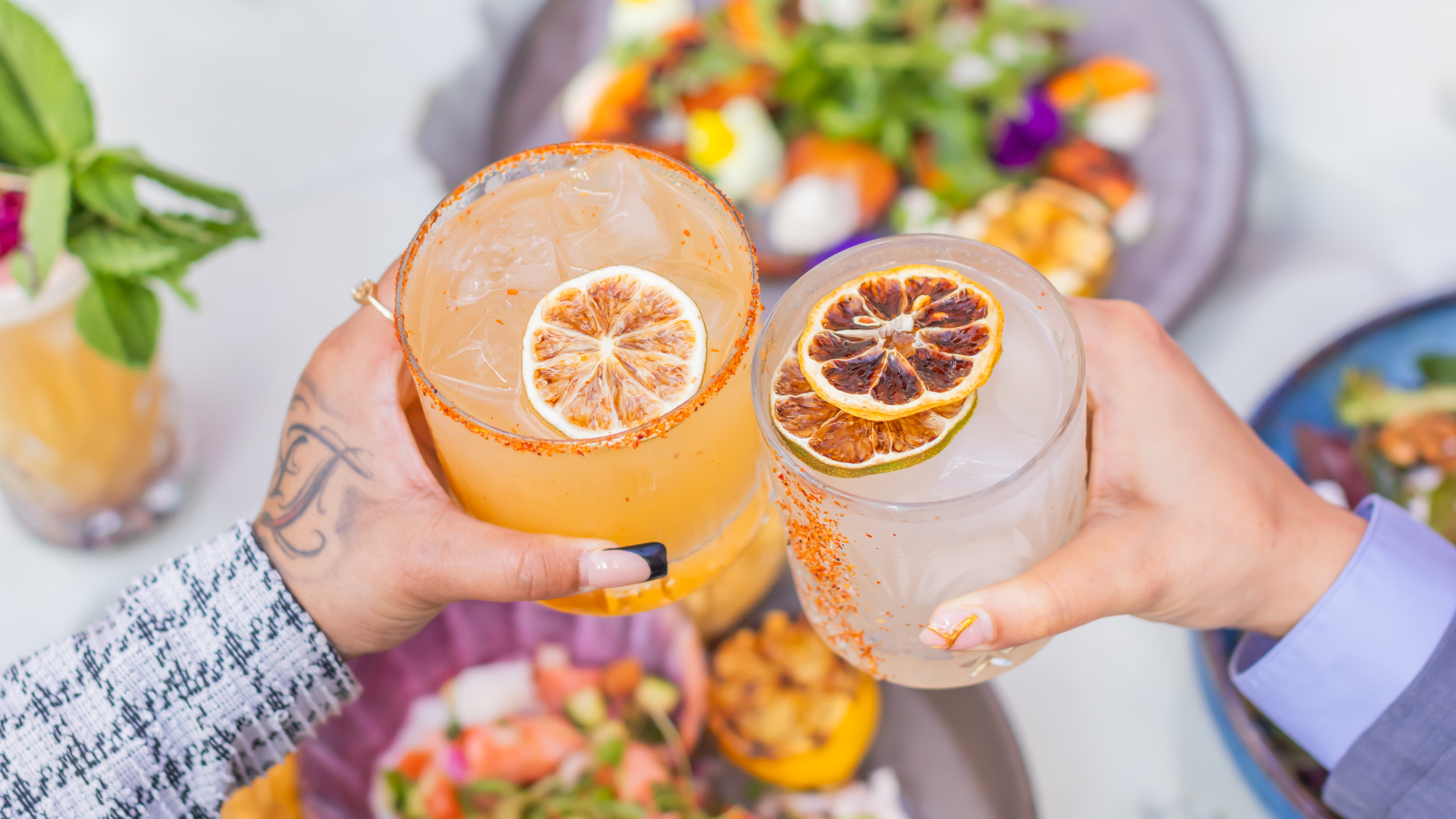 a pair of hands holding glasses with oranges and a slice of orange