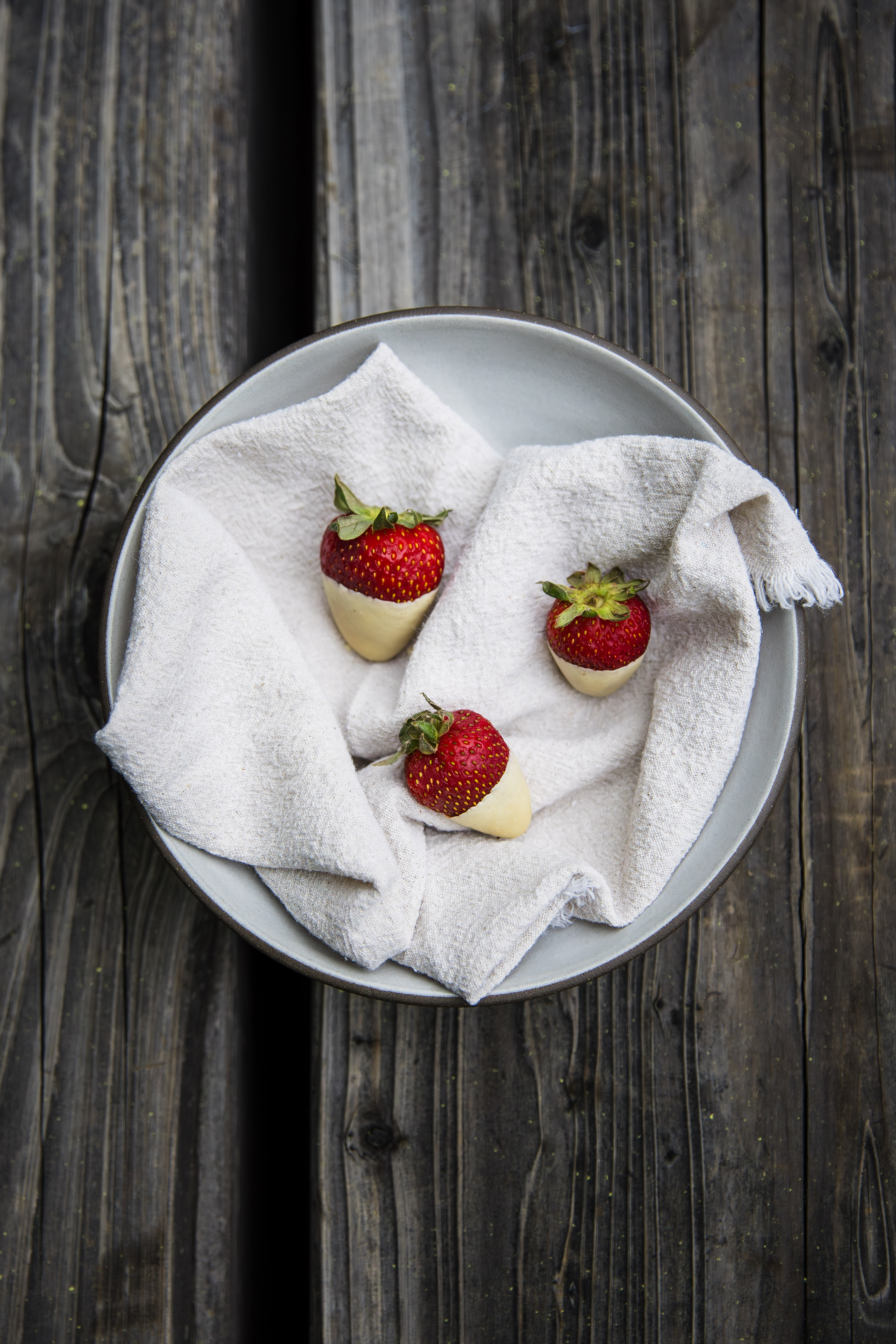 overhead image of a bowl of three strawberries dipped in white chocolate