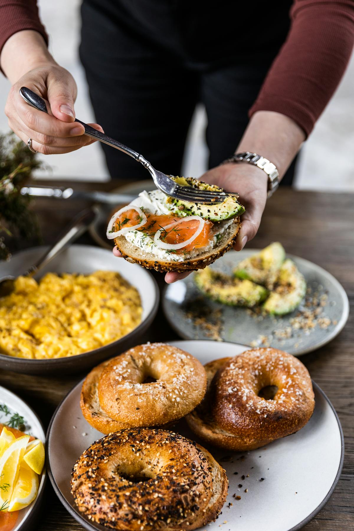 person adding lox, onions and other toppings to a bagel