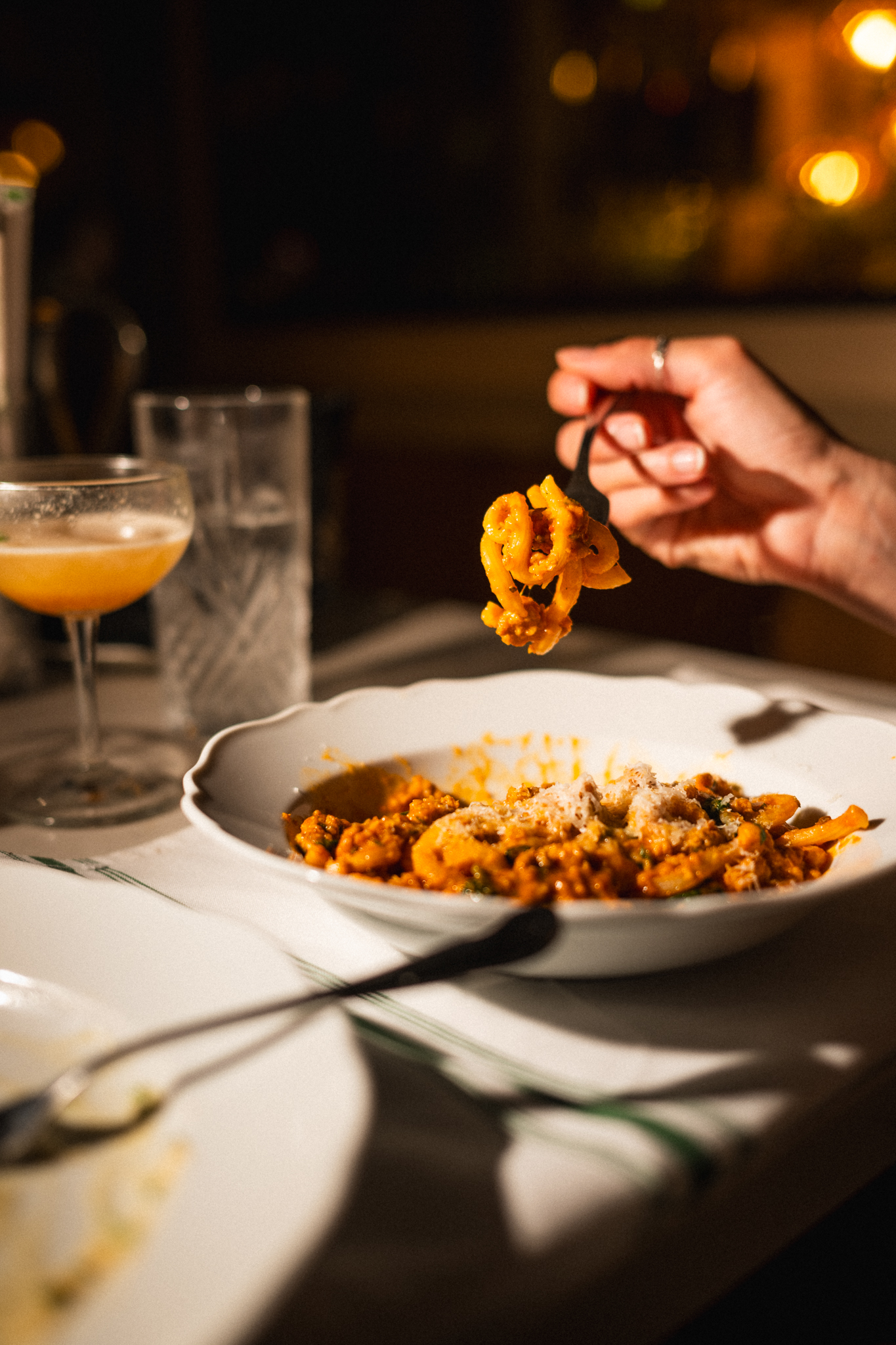 a hand holding a fork over a bowl of pasta