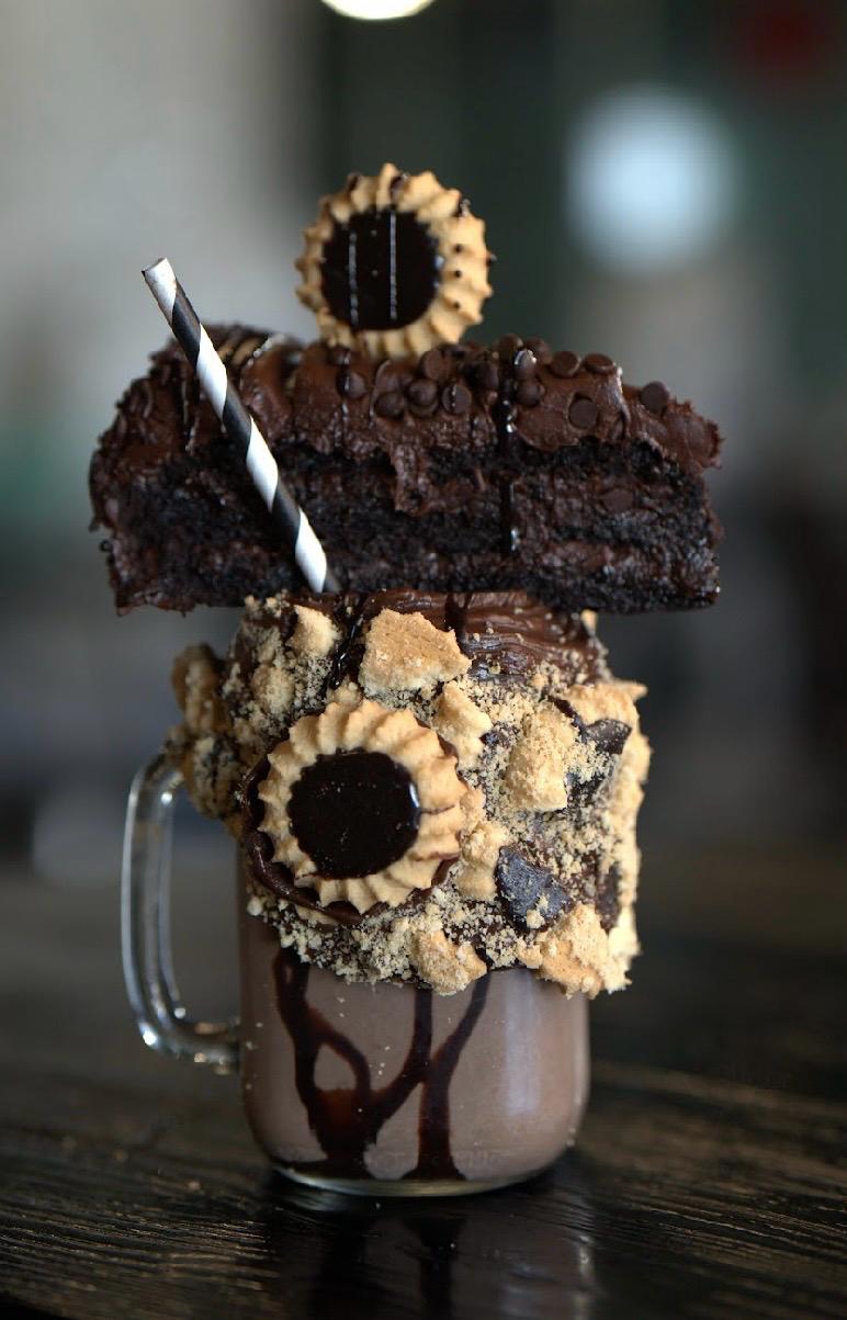 a chocolate milkshake with a slice of cake and cookies on top