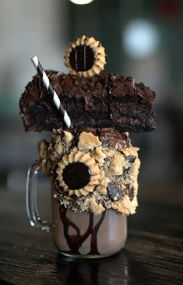 a chocolate milkshake with a slice of cake and cookies on top