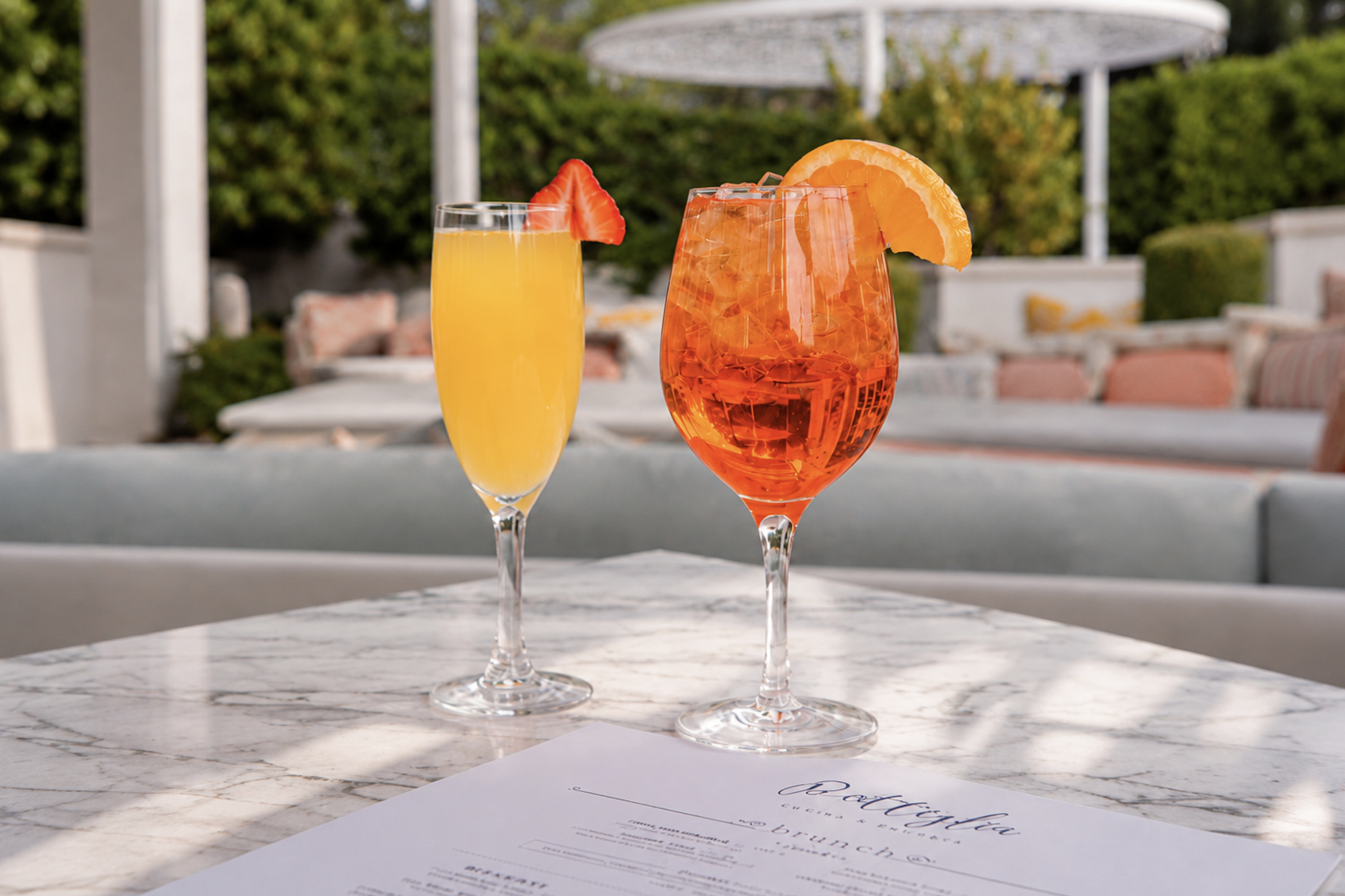 Two brunch cocktails—a yellow mimosa garnished with a strawberry and an orange spritz with an orange slice