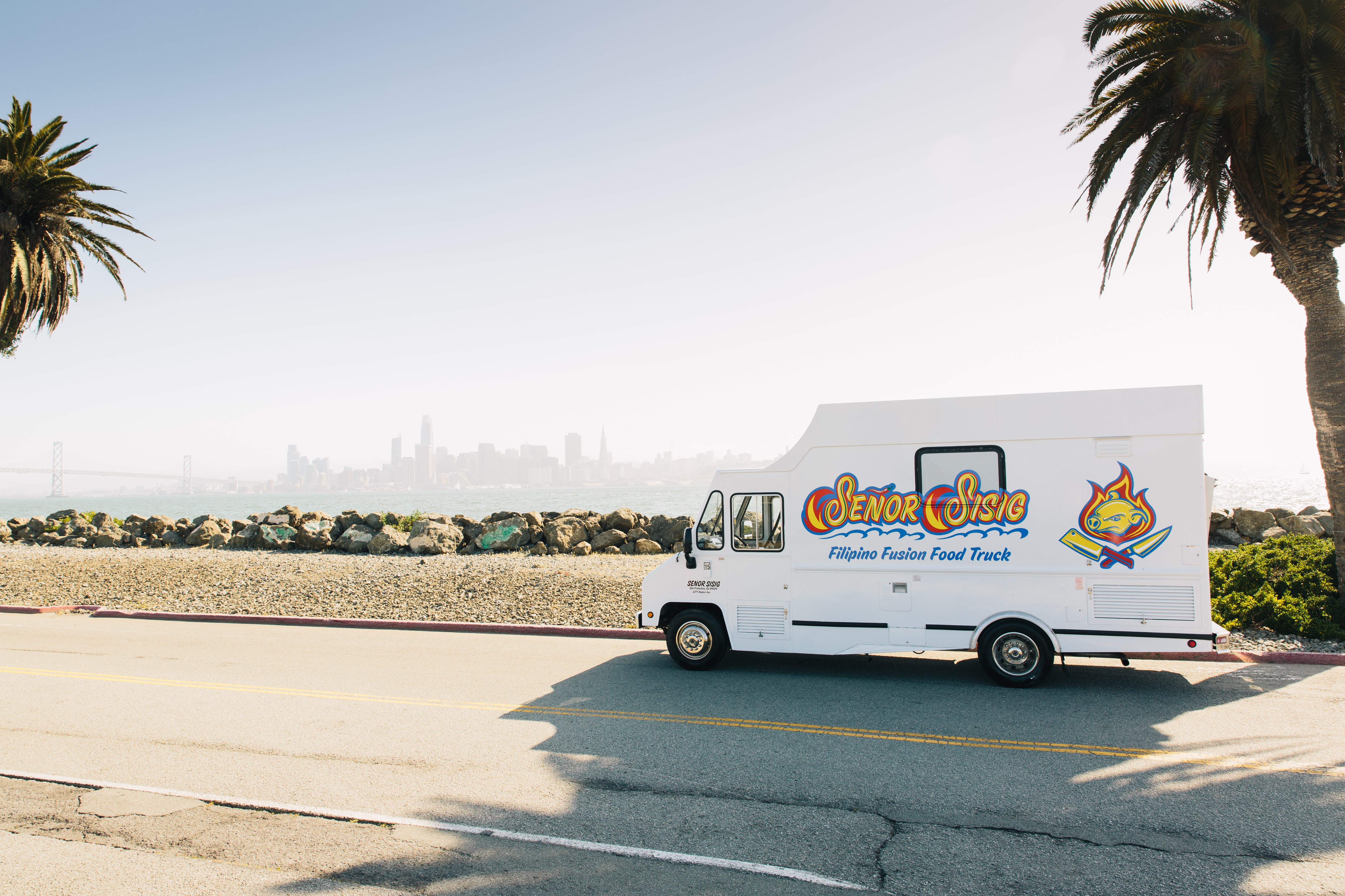 a food truck driving down a street next to a palm tree