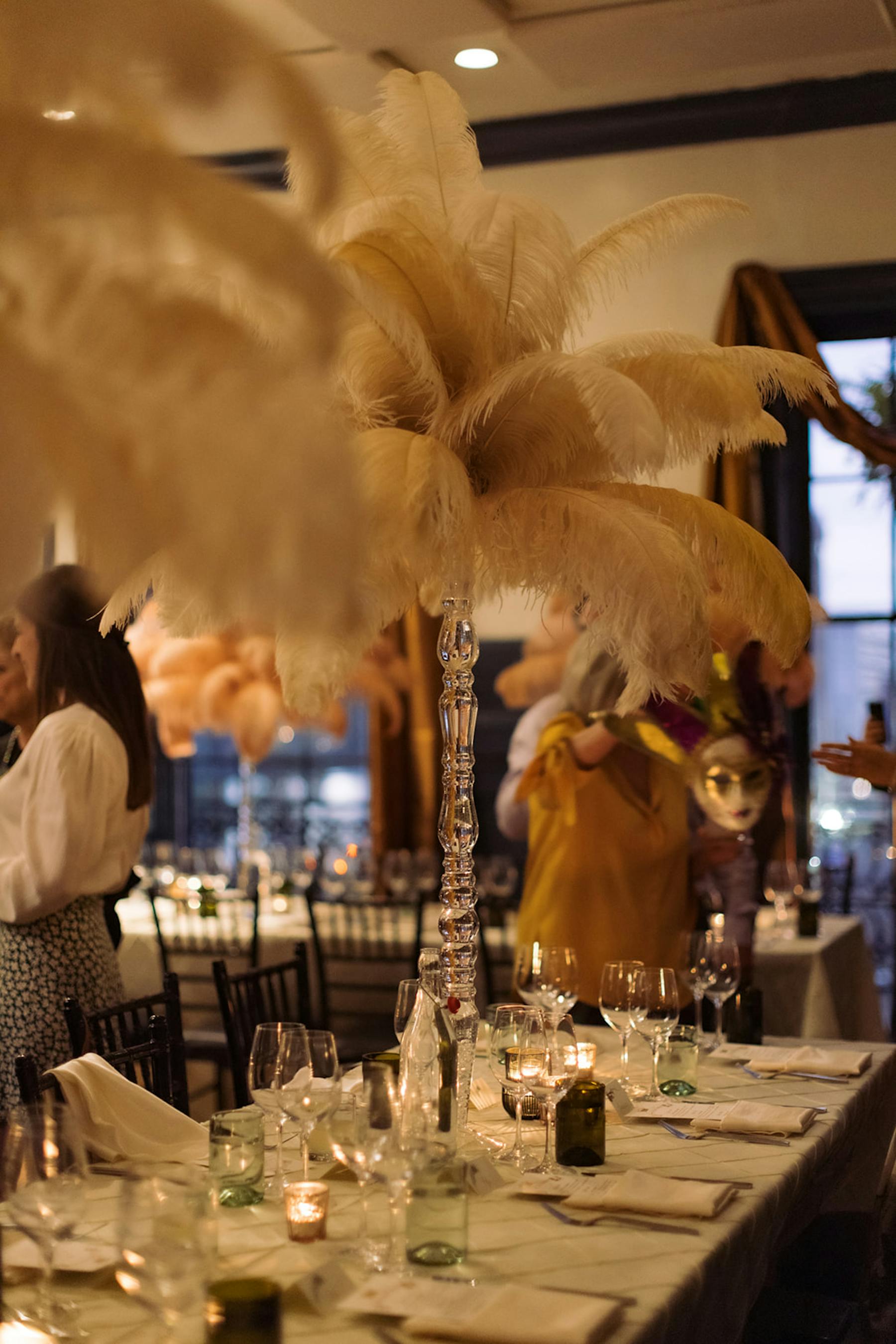 A beautifully set table with white tablecloths and an elegant large feather centerpiece