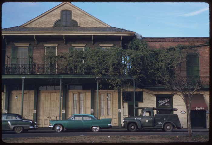 A two-story brick building with a gable roof and a tree in front of it.