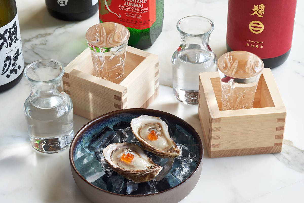 A Plate With Two Oysters With Glasses Of Sake And Bottles Of Alcohol To The Side