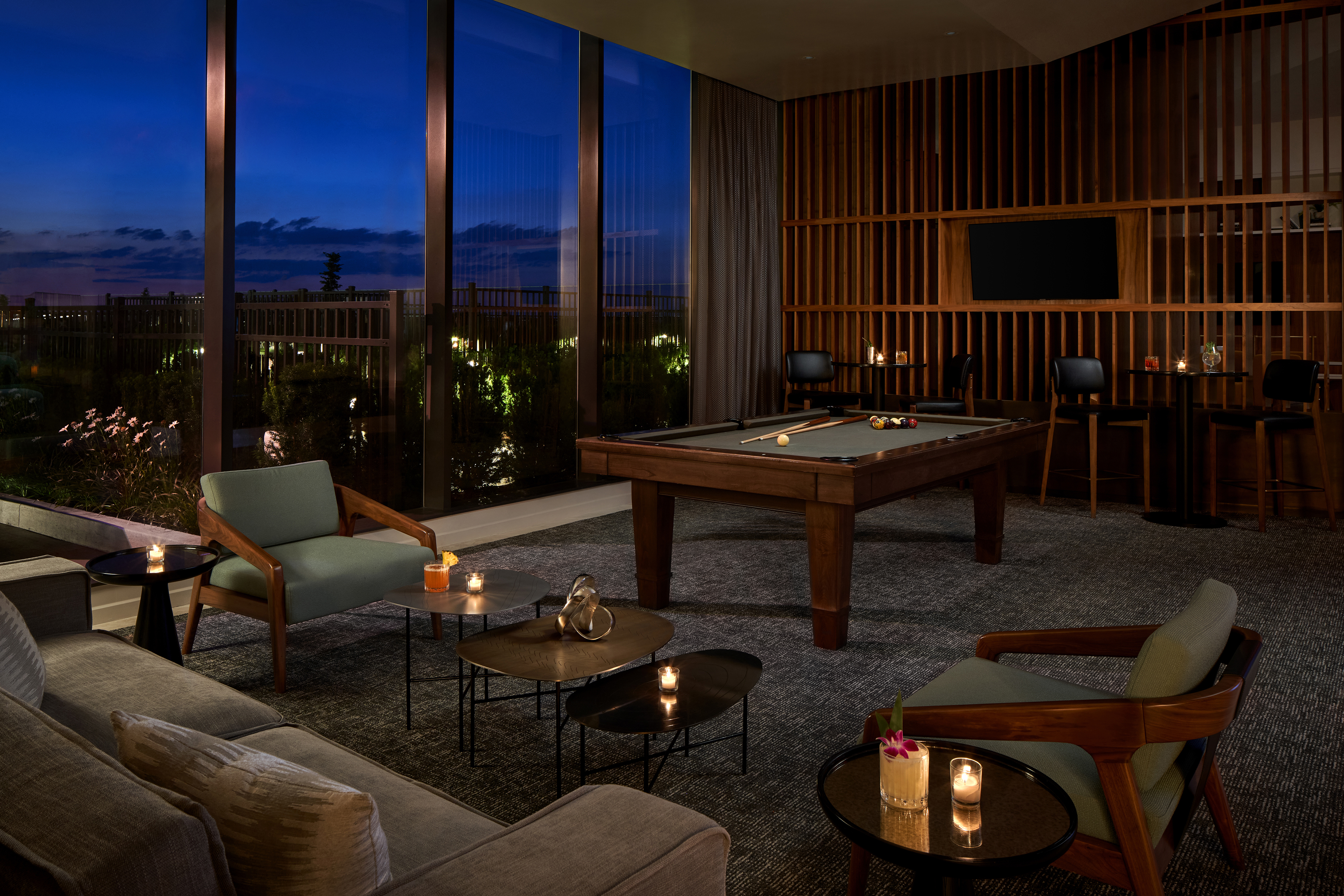 Lounge Chairs And Tables Topped With Cocktails In A Dimly Lit Room With A Pool Table In The Background