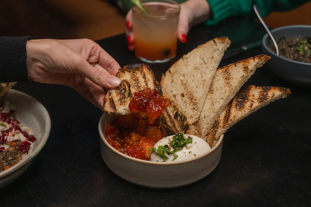 a person holding a piece of bread with a bowl of bread and a glass of juice