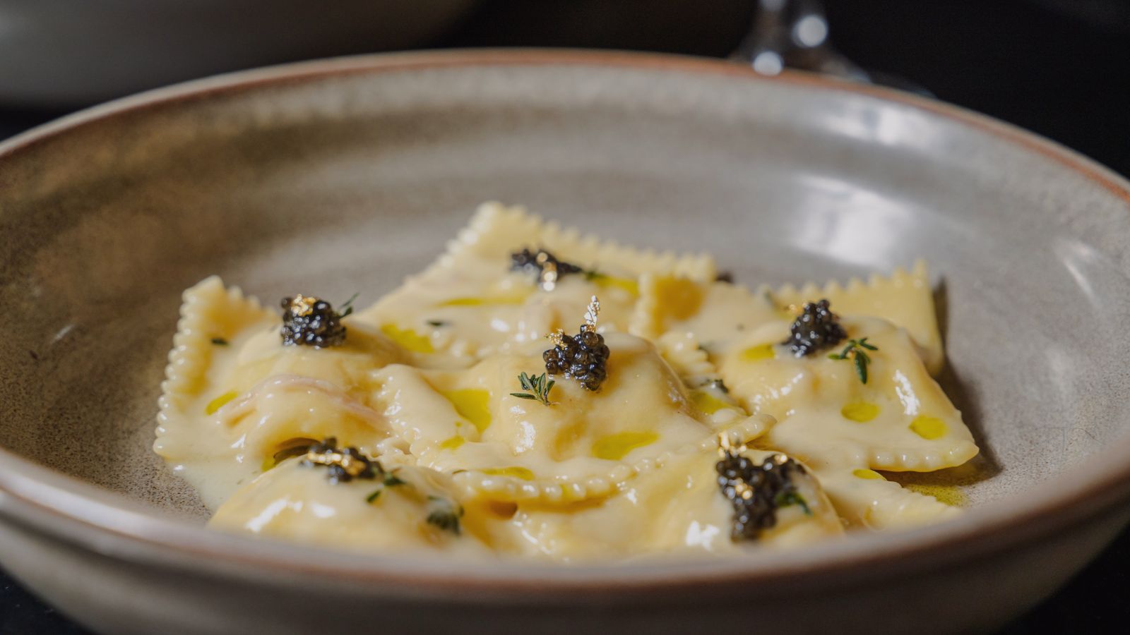 Ravioli topped with caviar and herbs in a shallow ceramic bowl.