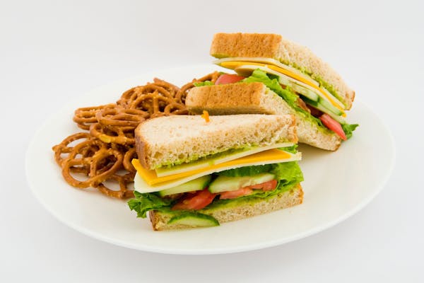 a sandwich cut in half sided with pretzels on a plate