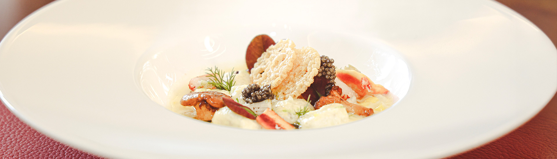 Image of seafood bisque with lobster, clams, rice cake, and caviar, in a white dish on a red placemat at The Bocuse Restaurant on CIA’s campus in Hyde Park, NY.