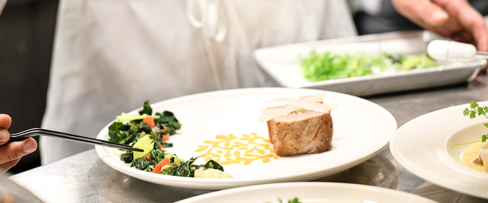 Image of A chef putting the final touches on a pork dish with vegetable medley at The Bocuse Restaurant on CIA’s campus in Hyde Park, NY.