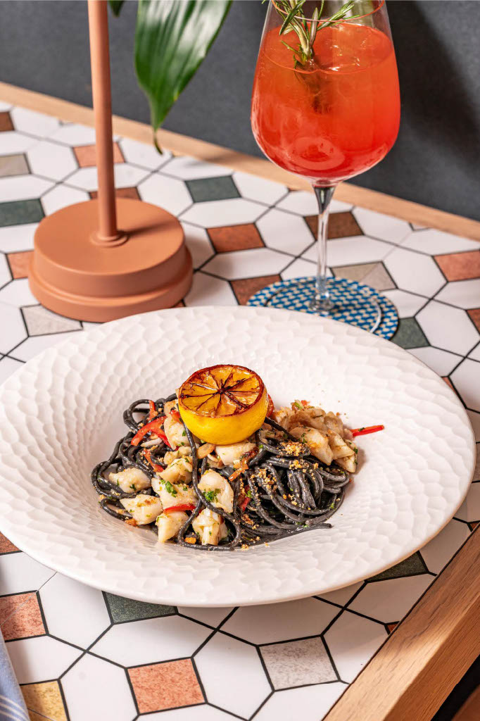a plate of black spaghetti with seafood and a lemon slice on top