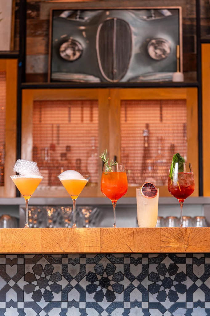 a row of different colored drinks on a bar