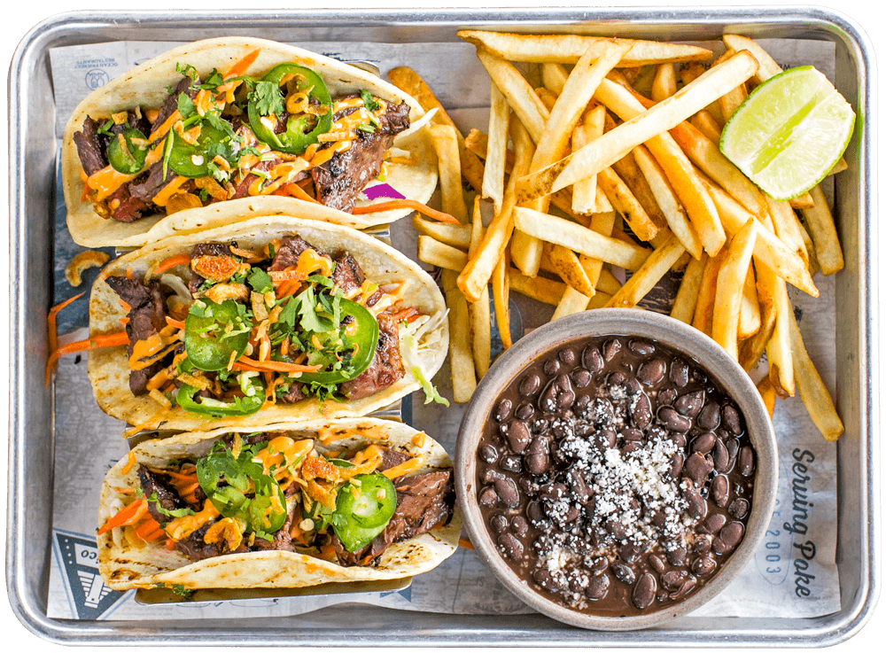 Three grilled steak tacos topped with jalapeños, cilantro, crispy onions, shredded vegetables and spicy sauce, served with fries, black beans and lime.