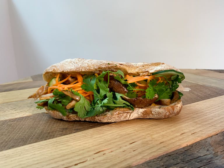 a Grilled Shiitake Banh Mi sandwich sitting on top of a wooden cutting board