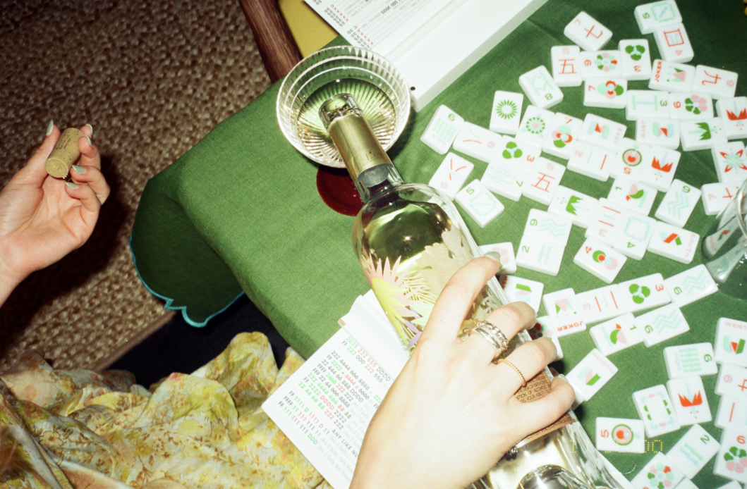 someone pouring a glass of wine on a table with mahjong tiles