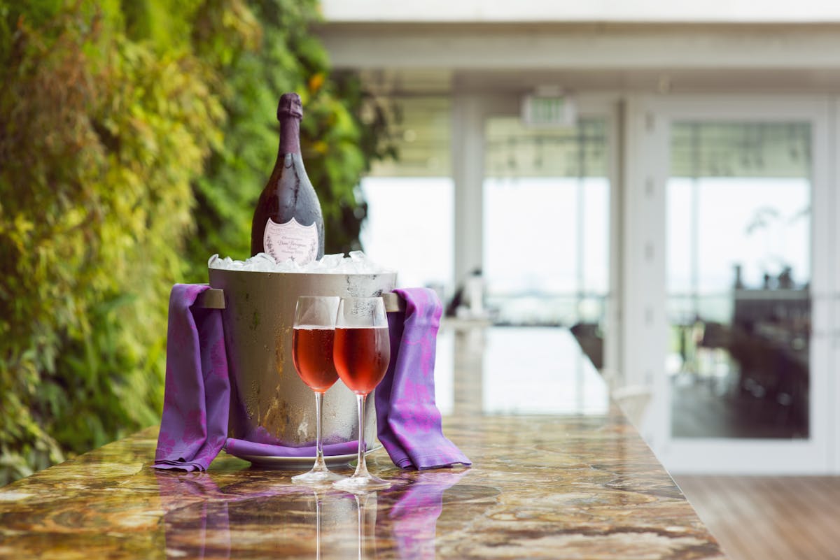 an ice bucket with a red wine within it sitting on a counter sided by two wine filled glasses
