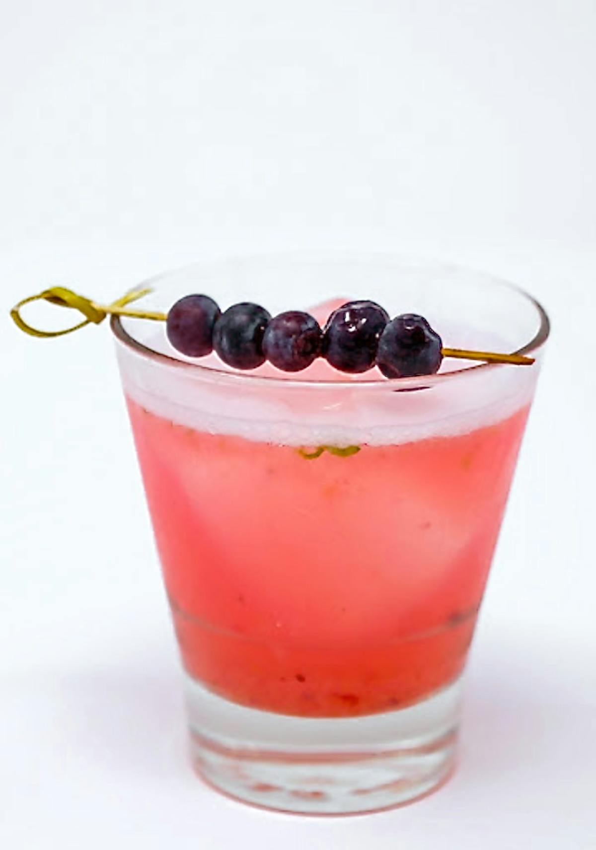 a close up of a pink drink topped with smaller skewer of blueberries