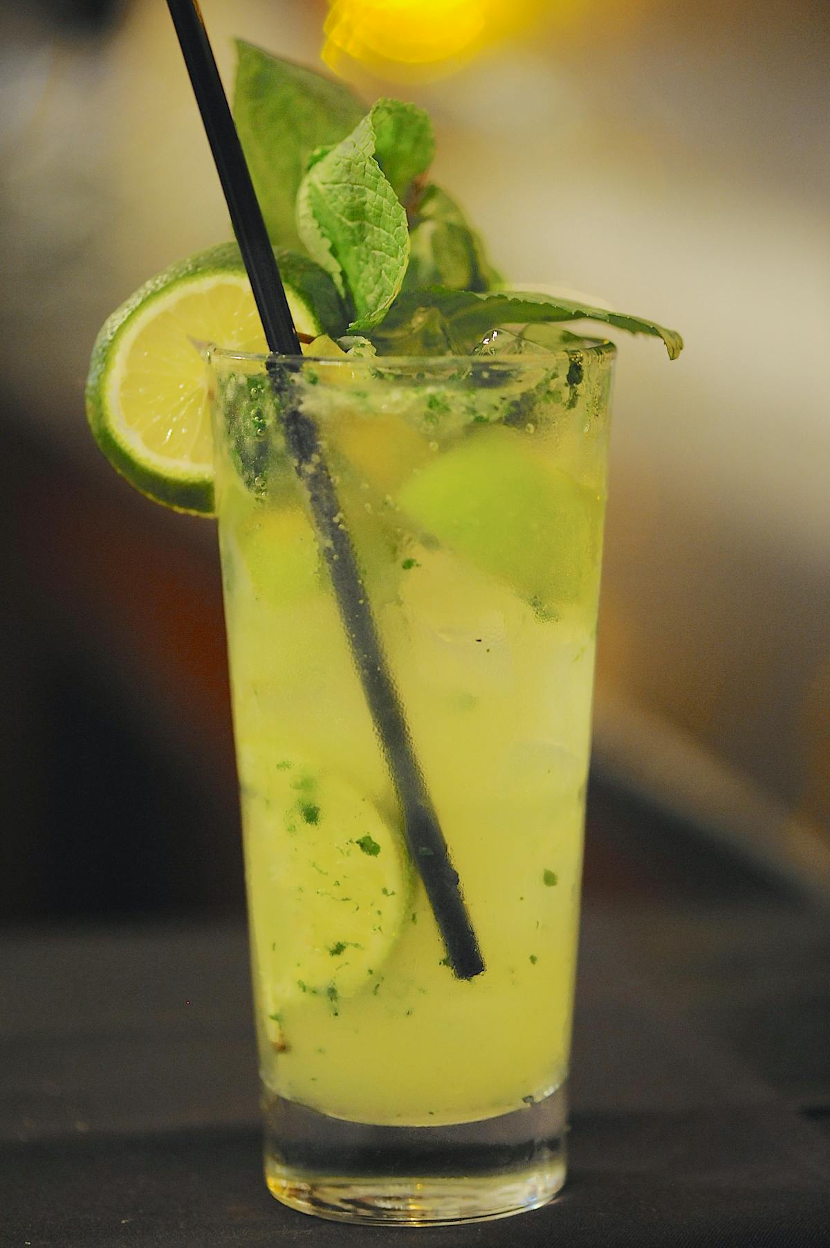 a close up of a lime yeloow drink with a few slices of lime within the drink topped with mint