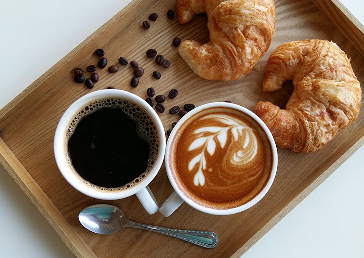 a cup of coffee and a doughnut sitting on top of a wooden table