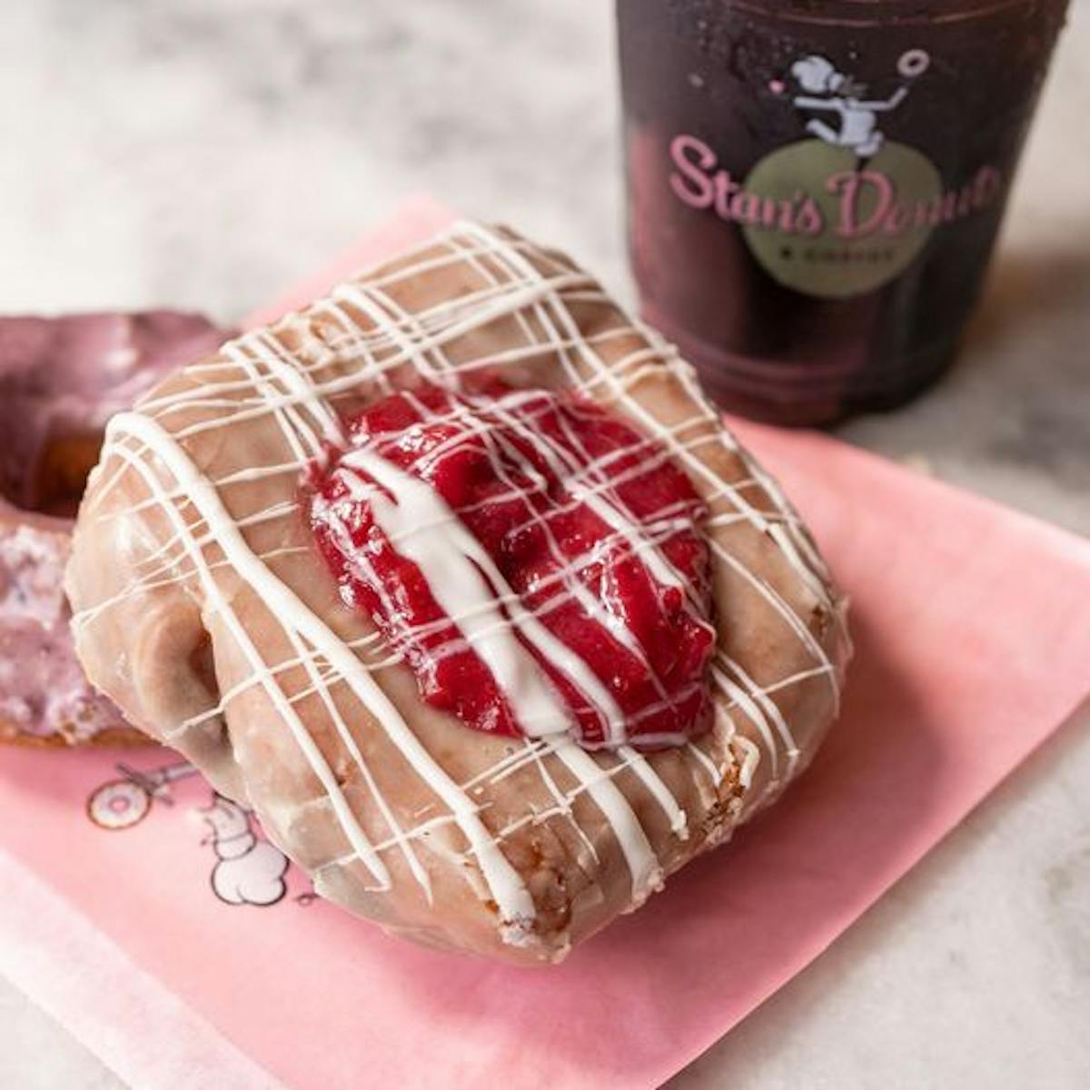 Cherry cream cheese pocket from Stan's Donuts sitting on a pink wrapper beside a clear plastic cup of coffee.