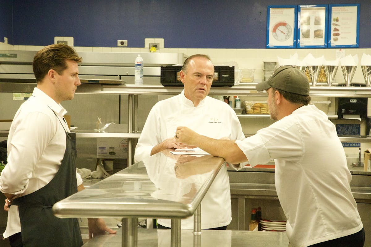 Charlie Palmer et al. standing in a kitchen preparing food