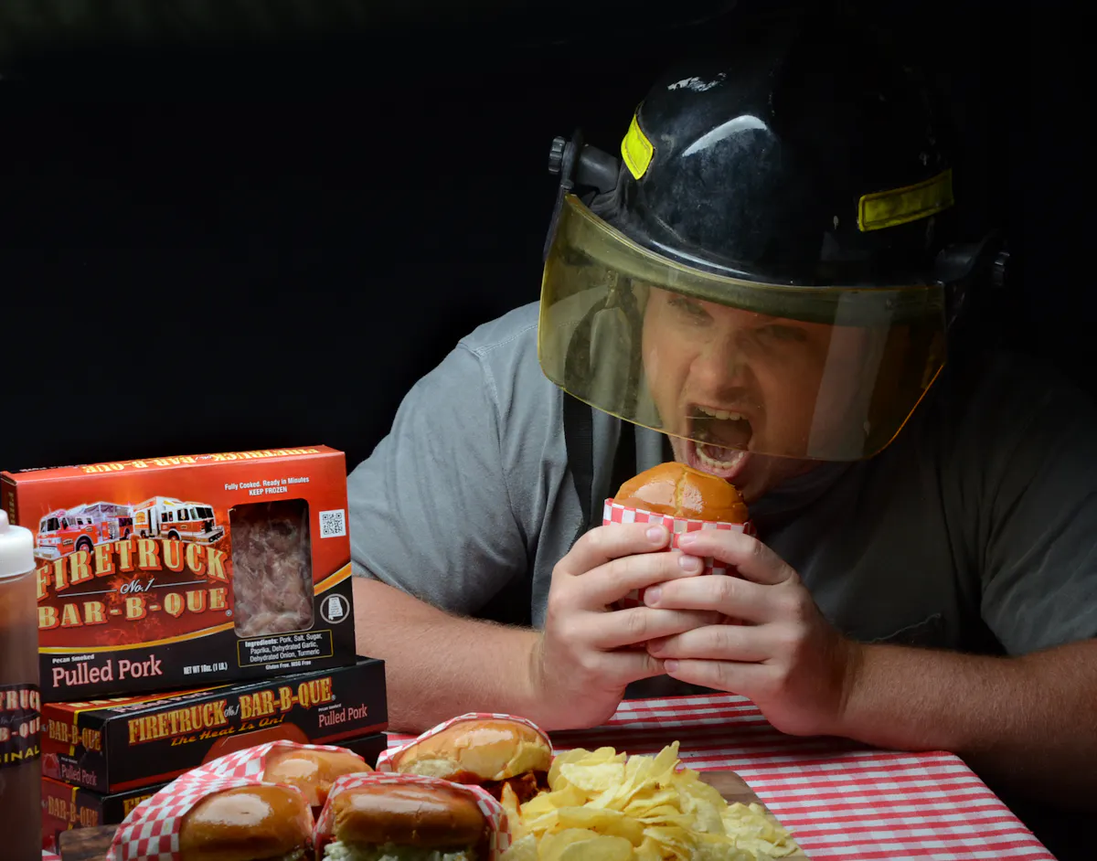 a man eating a hamburger using a fireman's hat