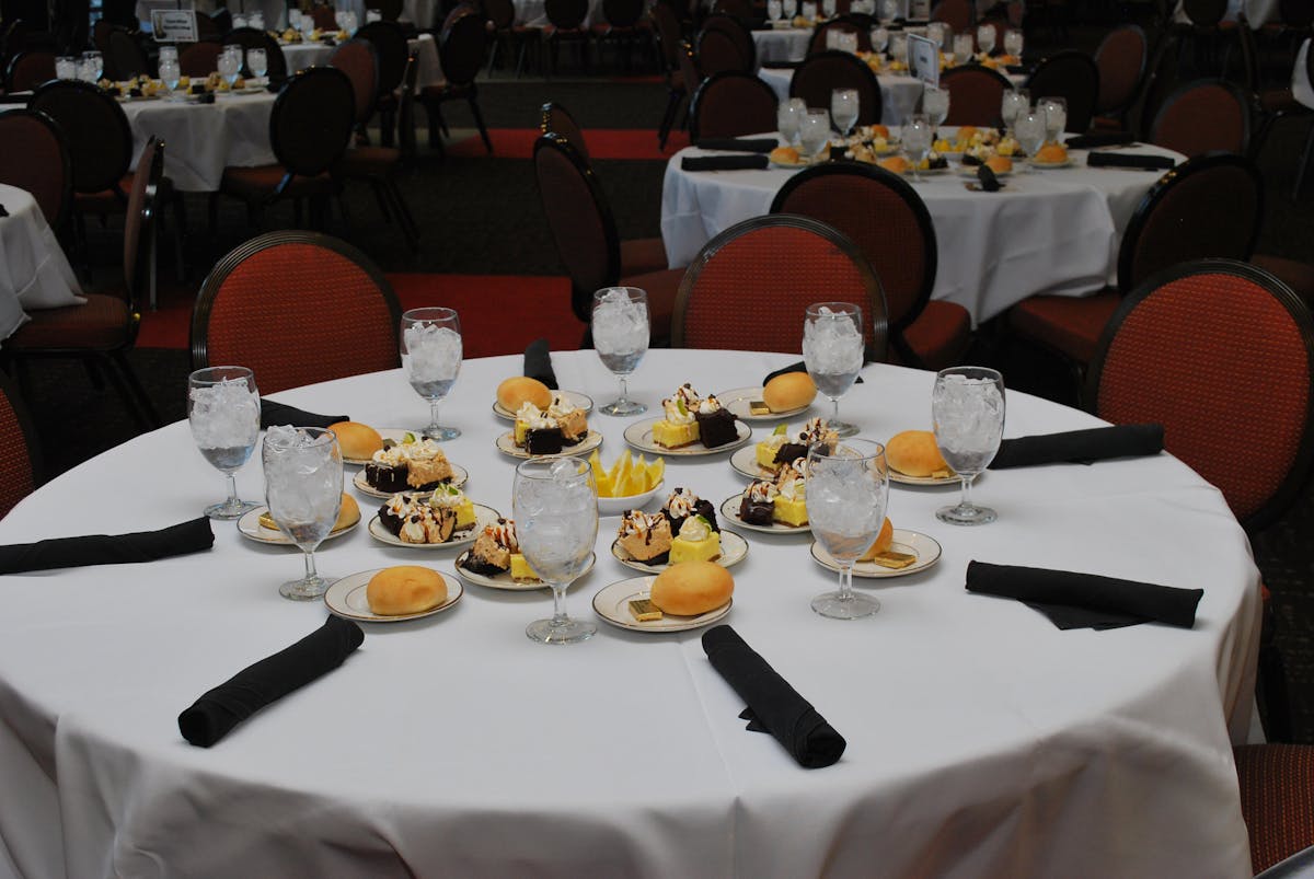 a round table with a white table cloth with desserts and bread plates with a glasses filled with ice